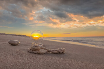 Ampoule posée sur le sable avec coucher de soleil sur le filament.	