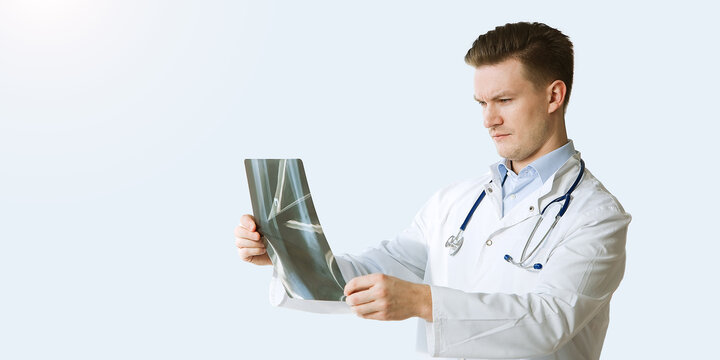Portrait of cheerful young medical doctor with stethoscope looking at x-ray  isolated over grey color background