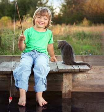 Happy boy go fishing on the river with cat, one children and pat of the fisher with a fishing rod on the shore of the lake