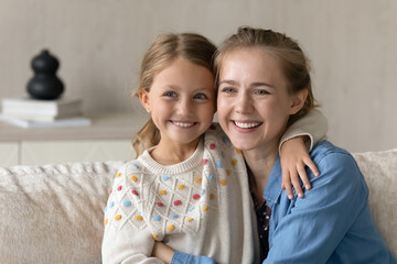 Happy bonding relaxed young mother and little kid daughter looking in distance, daydreaming thinking of good moments or watching TV series, sitting on couch, enjoying carefree peaceful moment at home.