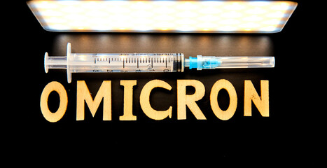 The word omicron made from wooden letters, syringe on a black background. Medical concept - Mutated...