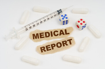 On a white surface lies a syringe, pills, dice and pieces of paper with the inscription - MEDICAL REPORT