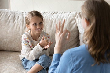 Happy cute little kid girl with hearing disability using sign language, communicating with caring...
