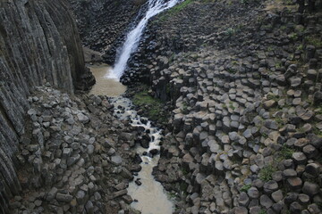 naturally formed basalt prisms have water coming from a stream that falls like a waterfall

