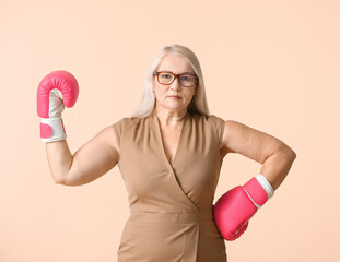 Mature woman in boxing gloves on color background. Concept of feminism