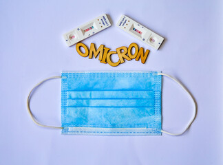 word omicron made from wooden letters, blue medical mask and 2 covid-19 antigen self-tests positive...