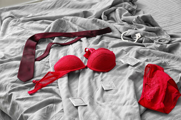 Male necktie and female lingerie with condoms and handcuffs on bed after romantic date