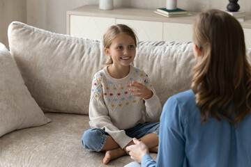 Happy adorable little kid girl sitting crossed legs on couch, doing vocal exercises or learning...
