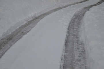 the road on the downhill is covered with a large amount of snow and traces of car tires