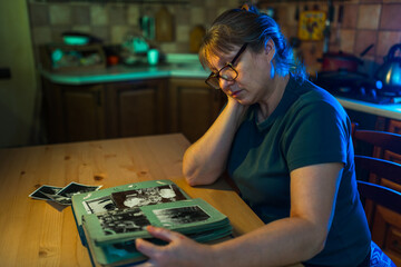 Fototapeta premium Middle aged woman looking at family photo album. Nostalgia, sadness, grief and memories at middle age concept.