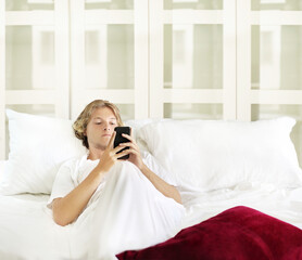 Young man relaxing on bed,using smartphone