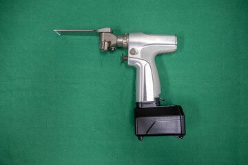 a battery powered surgical oscillating saw with saw blade lies on a green surgical drape