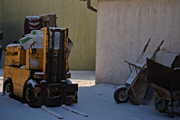 Stary wózek widłowy i taczki pokryte śniegiem.