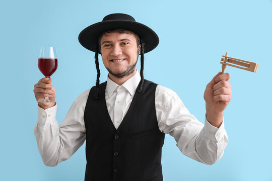 Young Jewish man with glass of wine and gragger for Purim holiday on color background