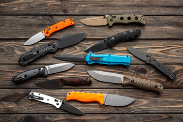 Folding knives and knives lie in a row on a brown wooden background. Various knives for hunting, sports and recreation on a wooden back