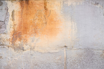 Fototapeta premium Damaged grey wall with orange paint splash texture background. Creative backdrop. Old building interior fragment. Weathered and cracked bricks with concrete and peeled off paint. Close up, copy space