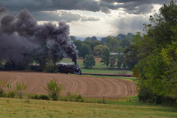 Fototapeta na wymiar An Antique Steam Engine Approaching With Passenger Coaches on an Overcast Fall Day