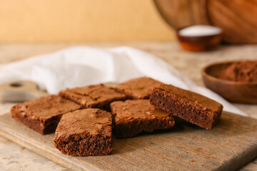 Wooden board with pieces of tasty chocolate brownie on beige background