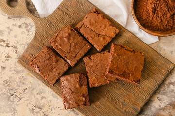 Wooden board with pieces of tasty chocolate brownie on beige background