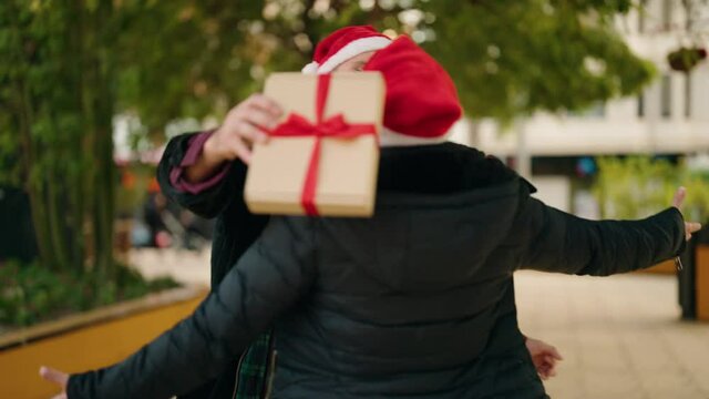 Mother and son wearing christmas hat surprise with gift at park