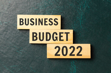 There is a blue notebook on a light gray background. Above are three wooden blocks with the words Business budget 2022