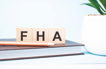 FHA acronym on building blocks supported by two different size pencils. Copy space.