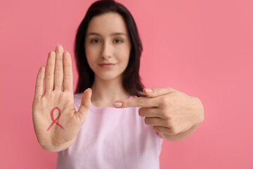 Young woman with ribbon on pink background. Breast cancer awareness concept