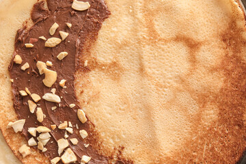 Tasty thin pancakes with chocolate paste and nuts as background, closeup