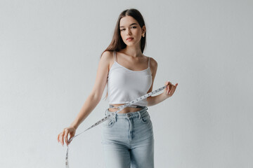 Young brunette woman with measuring tape and a beautiful, healthy body, looking at the camera. Beautiful woman measuring her perfect body