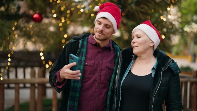 Mother and son wearing christmas hat make selfie by the smartphone at park