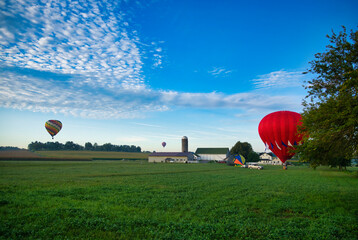 Obraz premium Multiple Hot Air Balloons Landing in Farmlands as Amish Look on, and More Still in Flight