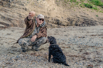 Happy senior citizen plays with dogs on the seashore against the backdrop of a cliff.