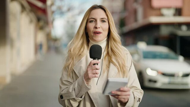 Young blonde woman journalist speaking using microphone at street