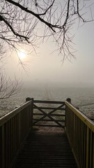 Wooden bridge with gate leading onto frosty winter field with a pathway fading into the distance on a chilly morning