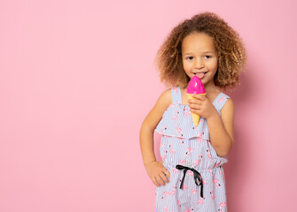 Cute little girl with curly hair holding ice cream standing isolated over pink background.