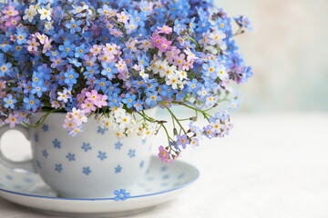 Bouquet of spring forget-me-not flowers in a cup on the table against the background of a colored...