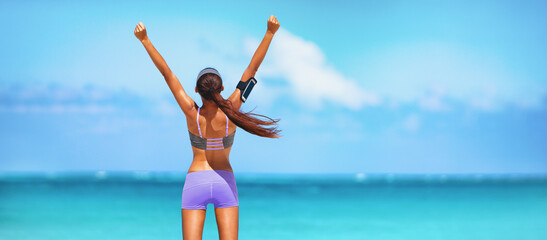 Goal achievement happy fitness woman with open arms in success for exercise challenge. Fit girl listening to podcast with phone and earphones view from the back banner panoramic.