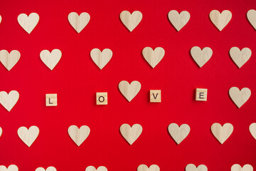 Postcard to Valentine's Day. The red background is filled with small wooden hearts made of natural wood and the word love in the center of the card