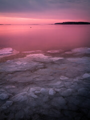 Frozen bay with pieces of broken ice floating in the Vineyard Sound shoreline illuminated by the pink sunrise rays.