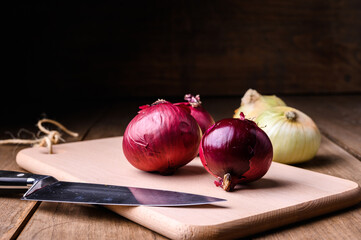 Red and white onions on a wooden chopping board and knife on a rustic wooden table in the kitchen, top view. High quality photo