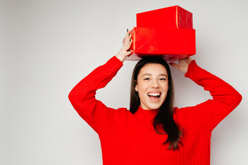 A young woman with a broad smile is standing against the white background. The girl is wearing a red sweater and holding red boxes on the head. Concept of the St. Valentine's Day