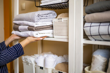 Domestic woman in pajamas neatly putting folded linens into cupboard vertical storage Marie Kondo