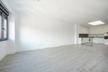 Large empty room with a kitchen at one end and a window at the other.
