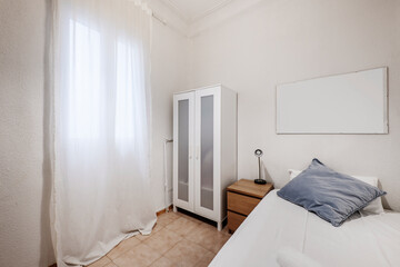 Shabby bedroom with white wardrobe and white drapery covering the window