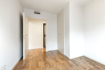 Empty bedroom with fitted wardrobe with white doors and painted walls with oak parquet flooring