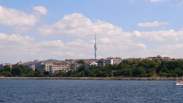 Green park along coast and buildings of Moda neighbourhood as seen from boat sailing by Marmara Sea. New Camlica TV Tower seen on background. Istanbul city views from water