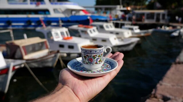 Tourist man enjoying his vacation on the islands of Istanbul stands on the waterfront with a cup of coffee. Fishing boats bobbing in the water along the shore. A passenger ferry has arrived in port