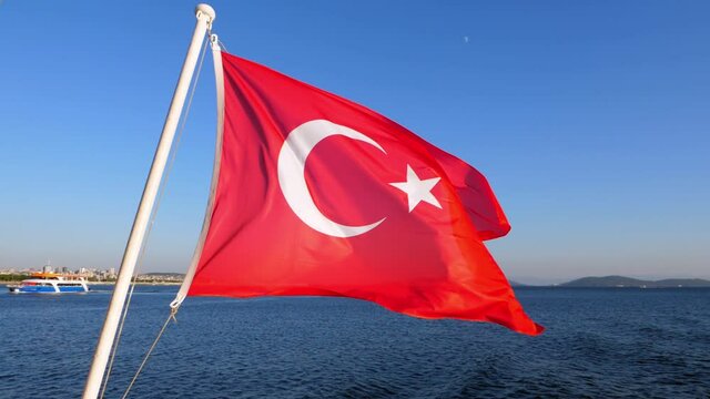 Bright red Turkish flag flutters in wind. Typical ensign at stern of ferry ship, slow motion shot. Calm Marmara Sea, Prince's Islands and Asian shore of Istanbul seen in the background
