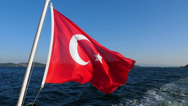 Turkish flag is flying in the wind against the background of Adalar and blue sky. Traditionally, the national symbol is hang at stern of every ferry in Istanbul