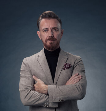Portrait of a stylish elegant senior businessman with a beard and casual business clothes in photo studio isolated on dark background gesturing with hands